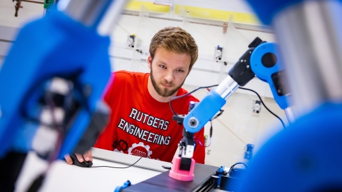 male wearing a Rutgers engineering t-shirt working with a blue robotic arm