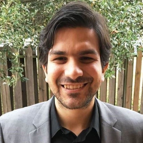 Smiling bearded man with dark brown hair wearing a grey suit jacket and black shirt