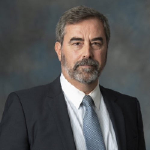 Headshot of white male with a beard wearing a dark suit, shite shirt, and blue tie