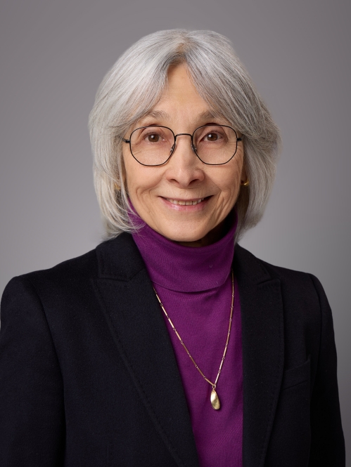 Headshot of female with short grey hair with bangs and eyeglasses wearing a purple turtleneck and black jacket.