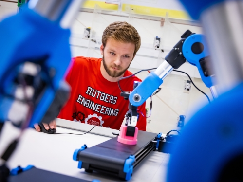 male wearing a Rutgers engineering t-shirt working with a blue robotic arm
