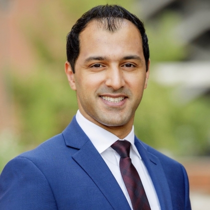 Headshot of smiling male wearing a blue suit, shite shirt, and maroon tie