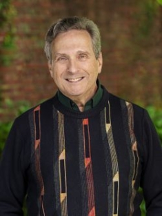 head shot of man with short hair wearing a black patterned button down shirt